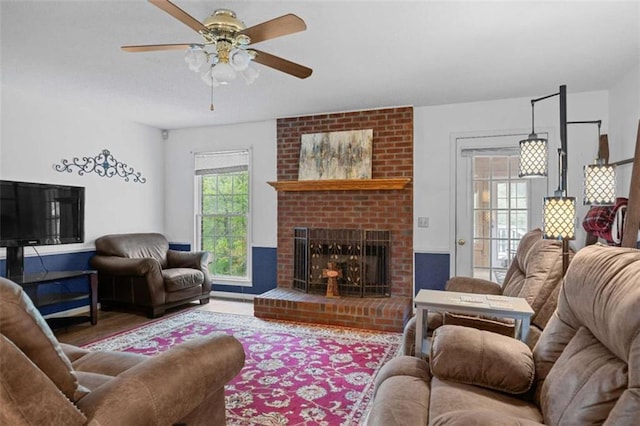 living area with ceiling fan, a brick fireplace, and wood finished floors