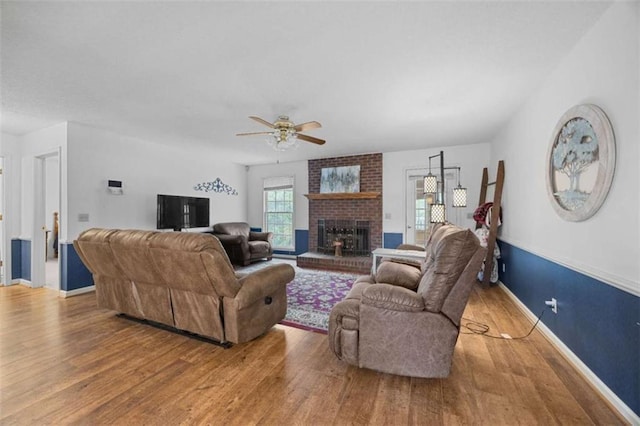living room featuring wood finished floors, a brick fireplace, baseboards, and ceiling fan