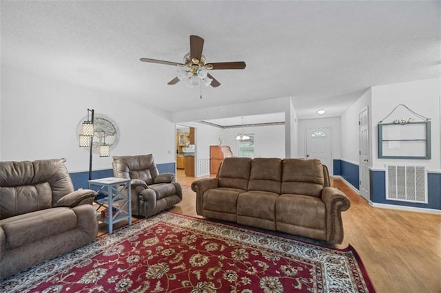 living room with a textured ceiling, wood finished floors, visible vents, and ceiling fan with notable chandelier