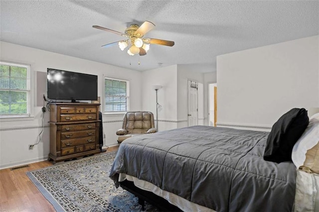bedroom with a baseboard heating unit, a textured ceiling, visible vents, wood finished floors, and ceiling fan