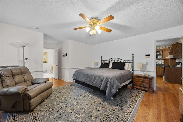 bedroom with ceiling fan, a textured ceiling, ensuite bathroom, and light wood-style flooring