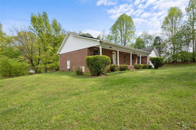 view of property exterior featuring brick siding, a porch, a yard, and fence