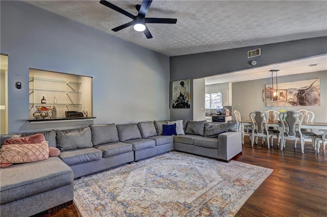 living room featuring visible vents, a ceiling fan, dark wood-style floors, vaulted ceiling, and a textured ceiling