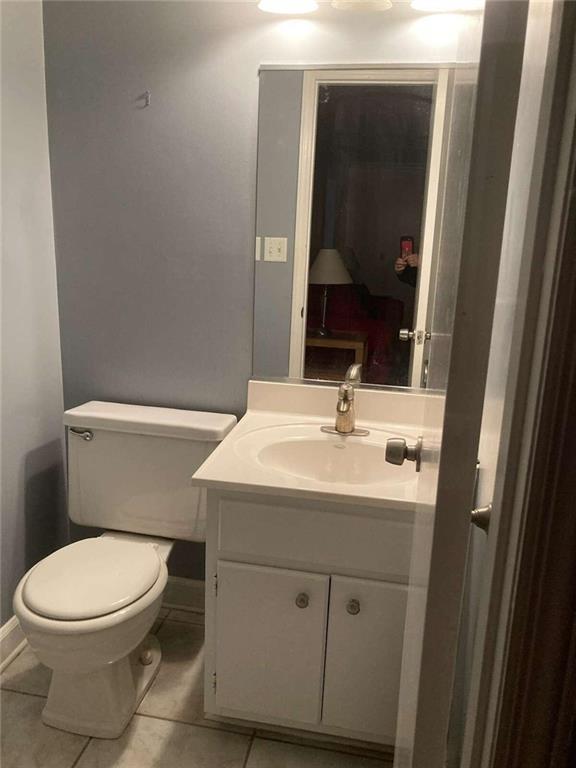 half bathroom with vanity, toilet, baseboards, and tile patterned floors
