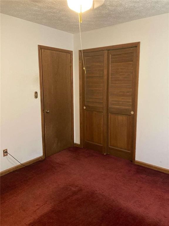 unfurnished bedroom with a textured ceiling, carpet flooring, a closet, and baseboards