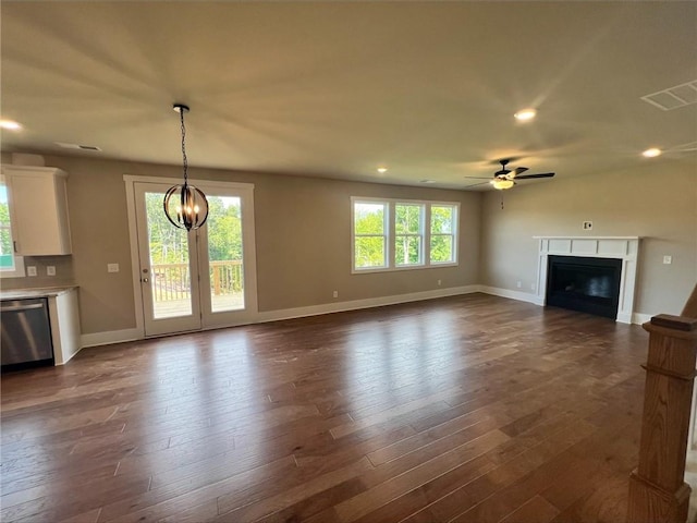 unfurnished living room featuring ceiling fan with notable chandelier, a wealth of natural light, and dark hardwood / wood-style floors