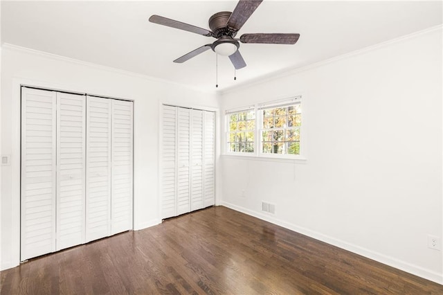 unfurnished bedroom with dark wood-type flooring, ceiling fan, crown molding, and two closets