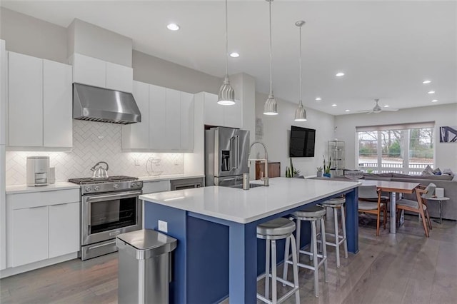 kitchen with white cabinetry, hanging light fixtures, range hood, a center island with sink, and high quality appliances