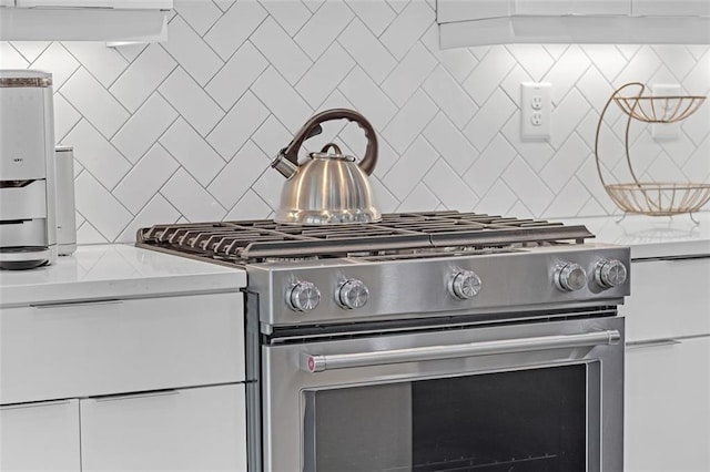 room details with light stone counters, white cabinets, tasteful backsplash, and stainless steel range with gas stovetop