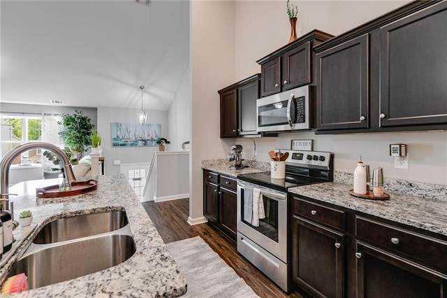 kitchen with appliances with stainless steel finishes, a sink, dark wood-style floors, dark brown cabinetry, and light stone counters