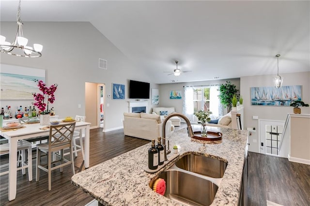 kitchen featuring a sink, a chandelier, dark wood-style flooring, a ceiling fan, and a fireplace