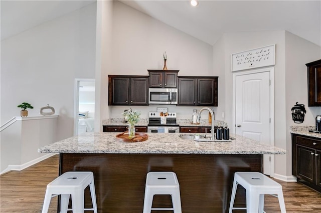 kitchen featuring stainless steel appliances, high vaulted ceiling, a kitchen bar, dark wood-style flooring, and baseboards