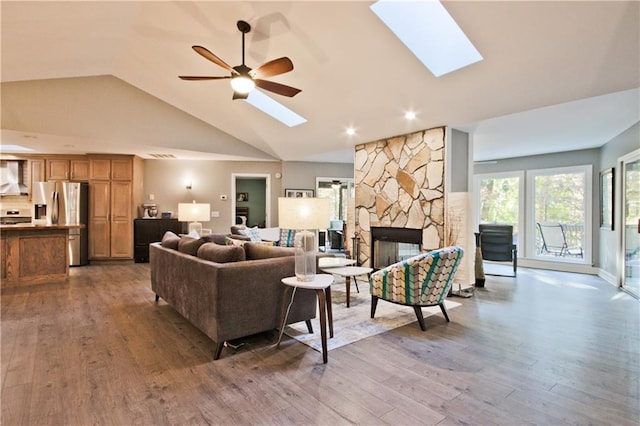 living room featuring wood-type flooring, a stone fireplace, and ceiling fan