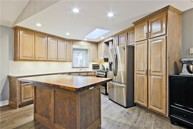 kitchen featuring butcher block countertops, wall chimney exhaust hood, light hardwood / wood-style floors, and appliances with stainless steel finishes