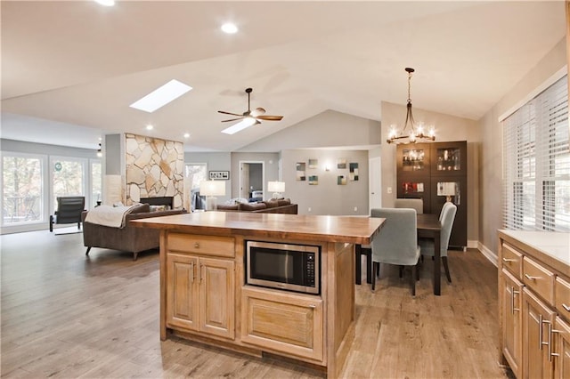 kitchen featuring butcher block countertops, stainless steel microwave, light hardwood / wood-style flooring, and vaulted ceiling