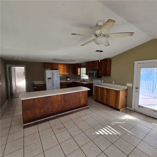 kitchen featuring a sink, stainless steel microwave, white refrigerator with ice dispenser, a kitchen island, and light tile patterned floors