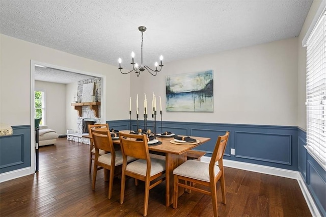 110 Village Ct, Woodstock, GA 30188 - dining room with a chandelier, dark wood-style floors, a wainscoted wall, a textured ceiling, and a stone fireplace