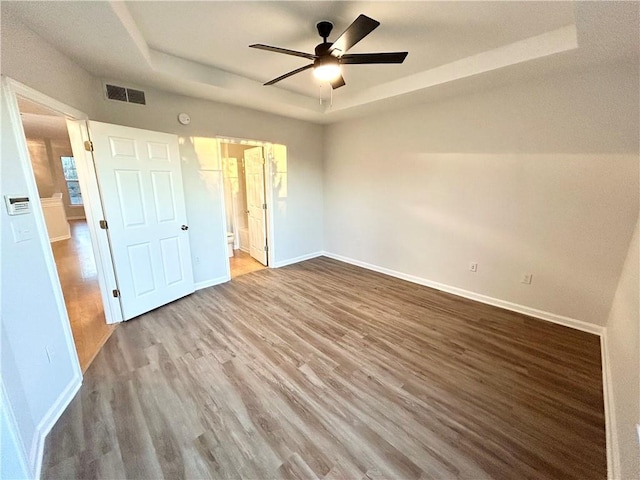 unfurnished bedroom with ceiling fan, wood-type flooring, connected bathroom, and a raised ceiling