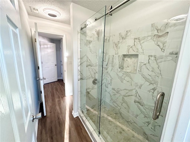 bathroom with wood-type flooring, an enclosed shower, and a textured ceiling