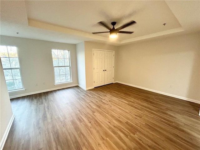 unfurnished bedroom with multiple windows, dark hardwood / wood-style floors, and a tray ceiling