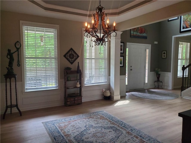 foyer featuring a raised ceiling, a healthy amount of sunlight, an inviting chandelier, and wood finished floors