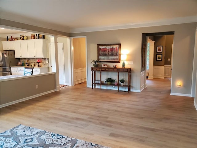 living area with a decorative wall, a wainscoted wall, decorative columns, light wood-type flooring, and crown molding