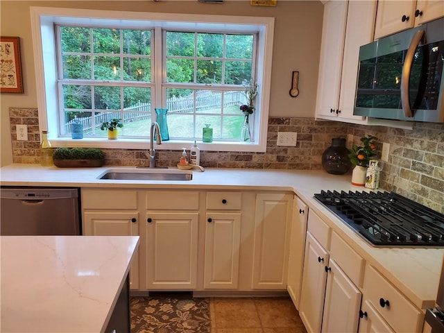 kitchen with light stone counters, a sink, backsplash, stainless steel appliances, and white cabinets