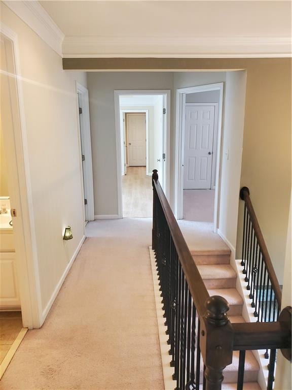 hallway featuring baseboards, ornamental molding, an upstairs landing, and light colored carpet
