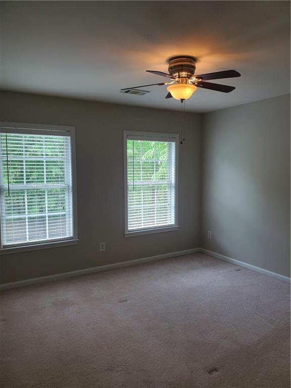 carpeted spare room featuring baseboards, a ceiling fan, and visible vents