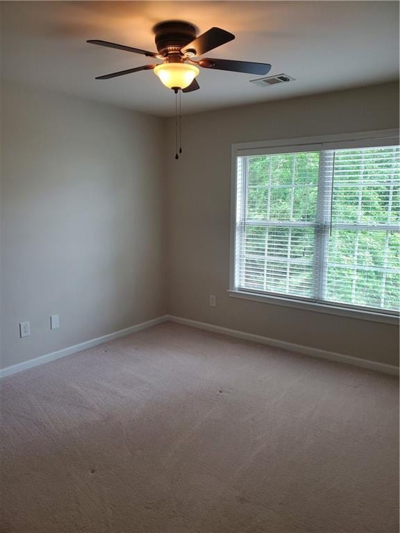 spare room featuring light colored carpet, ceiling fan, and baseboards