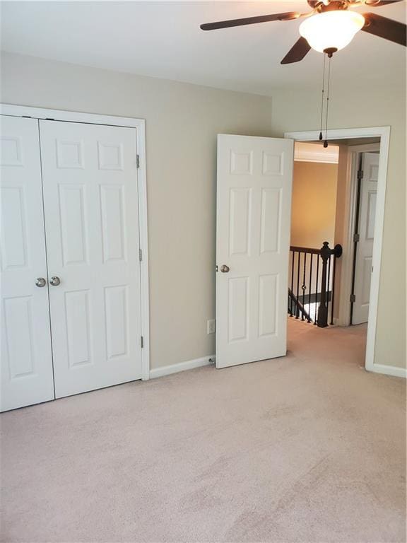 unfurnished bedroom with light colored carpet, a closet, baseboards, and ceiling fan