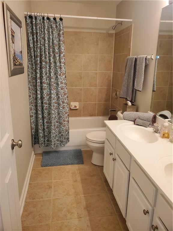 bathroom featuring a sink, toilet, shower / bath combo with shower curtain, tile patterned floors, and double vanity