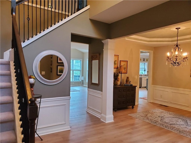 entryway featuring stairs, a decorative wall, a wainscoted wall, wood finished floors, and ornate columns