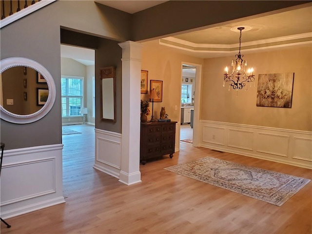 interior space with ornate columns, a notable chandelier, a decorative wall, wainscoting, and light wood-style floors