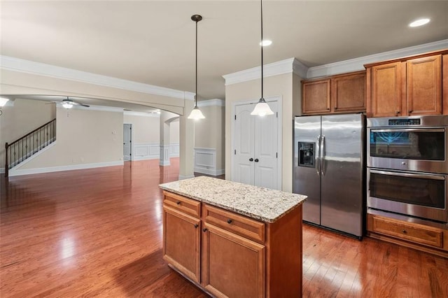 kitchen with pendant lighting, dark wood-type flooring, appliances with stainless steel finishes, light stone counters, and a kitchen island