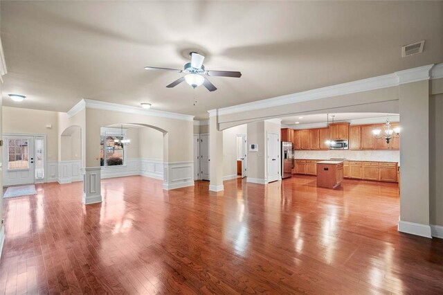 unfurnished living room featuring ceiling fan with notable chandelier, wood-type flooring, and ornamental molding