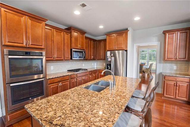 kitchen featuring tasteful backsplash, a breakfast bar area, stainless steel appliances, and a center island with sink