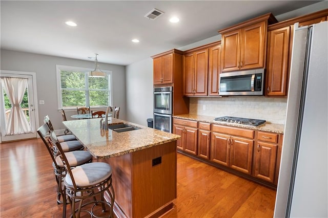 kitchen featuring pendant lighting, sink, appliances with stainless steel finishes, backsplash, and a center island with sink