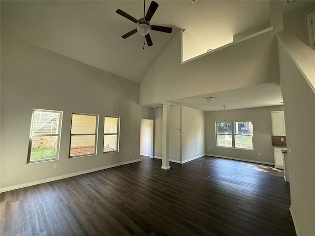 unfurnished living room with high vaulted ceiling, dark wood finished floors, a ceiling fan, and baseboards