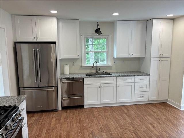 kitchen with a sink, light wood-style floors, stainless steel appliances, and white cabinetry
