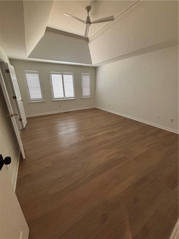 unfurnished room with baseboards, a tray ceiling, dark wood-style floors, and ceiling fan