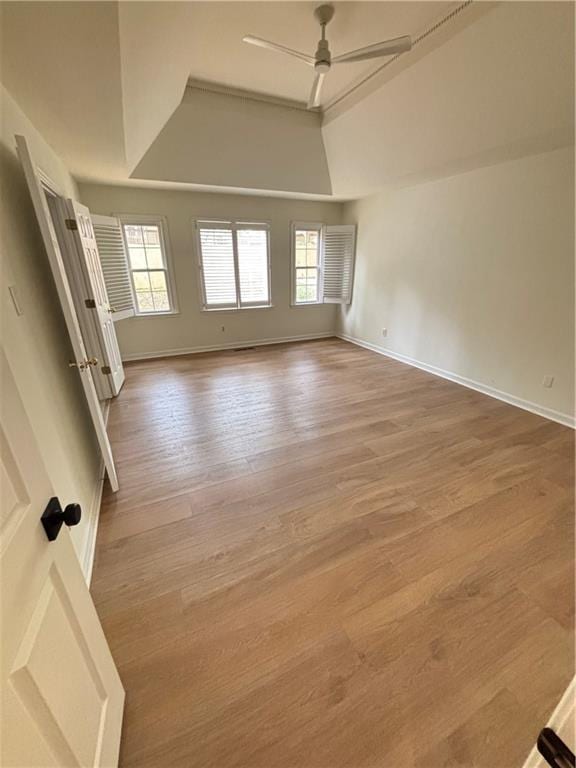 spare room featuring a raised ceiling, ceiling fan, baseboards, and wood finished floors