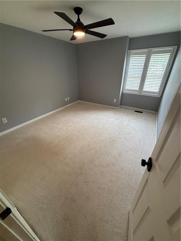 spare room with baseboards, ceiling fan, and light colored carpet