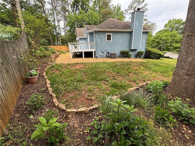 rear view of house with fence, central air condition unit, a wooden deck, a chimney, and a lawn