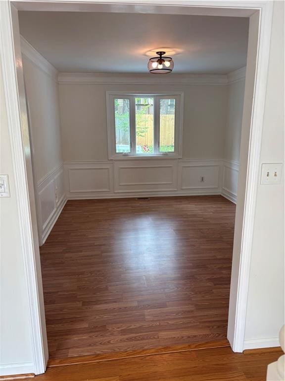 unfurnished room with wainscoting, ornamental molding, wood finished floors, and a decorative wall