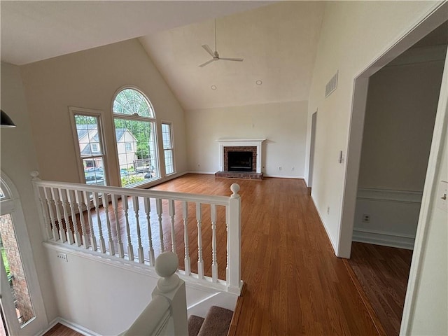 living room with a ceiling fan, visible vents, a brick fireplace, wood finished floors, and high vaulted ceiling