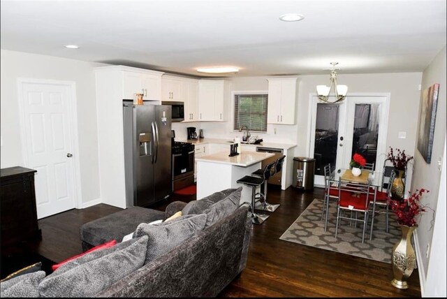 kitchen with white cabinetry, appliances with stainless steel finishes, hanging light fixtures, a kitchen island, and dark wood-type flooring