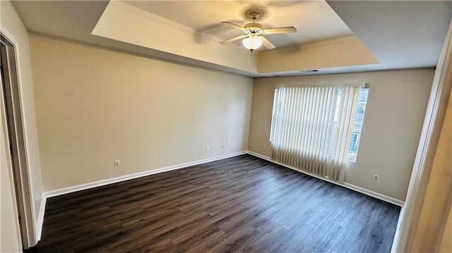 empty room featuring a raised ceiling, crown molding, ceiling fan, and dark wood-type flooring