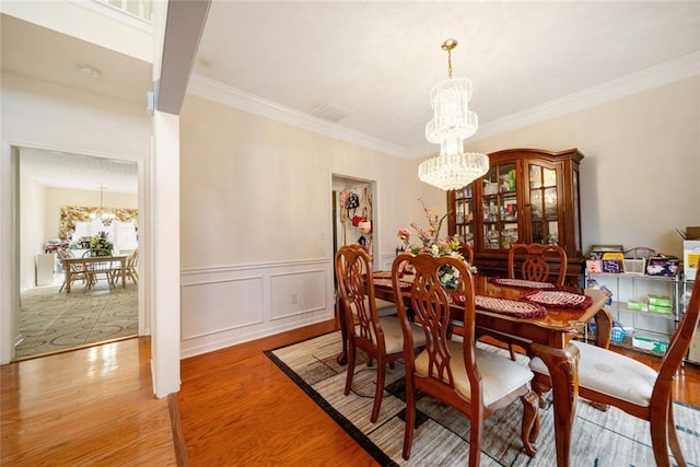 dining area featuring crown molding, wainscoting, light wood-type flooring, and a notable chandelier