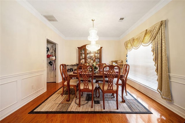 dining room with an inviting chandelier, crown molding, visible vents, and wood finished floors